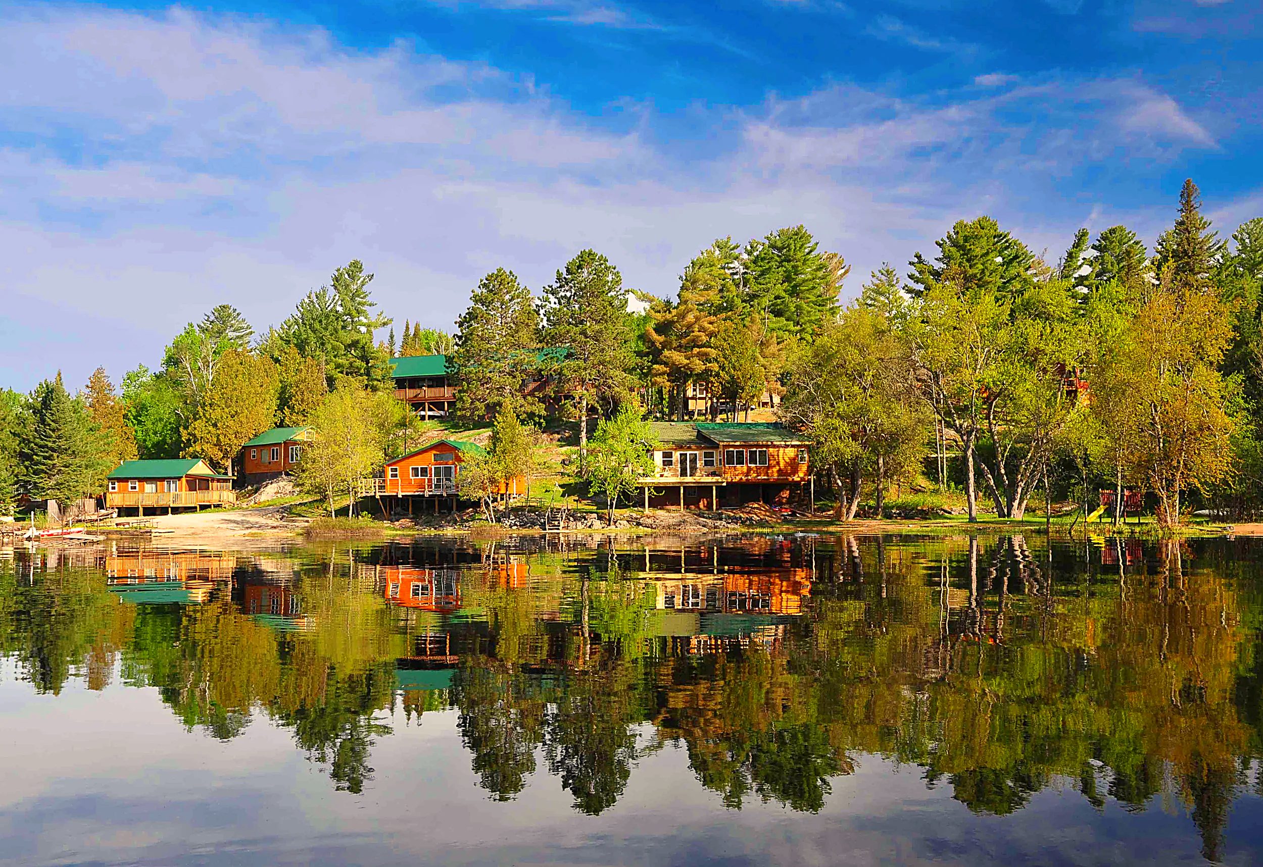 The cabins of Retreats on White Iron Lake reflected in the calm morning lake among the pines
